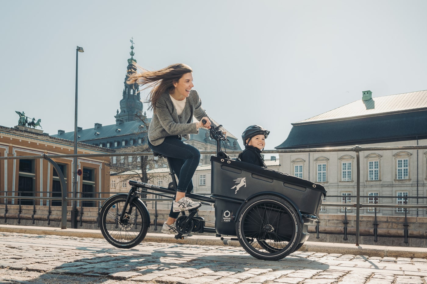 a woman riding a 3-wheel cargo bike with a child in Copenhagen